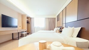 Quarto de hotel com uma cama grande, uma secretária com cadeira, televisão de tela plana e uma mesa com chá e utensílios.