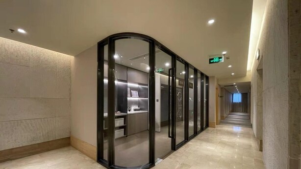 Um corredor moderno com um painel de vidro curvo que dá para um espaço com prateleiras e uma porta.