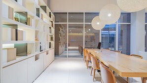 Um interior moderno com uma mesa de madeira comprida e cadeiras, estantes brancas e um painel de vidro.