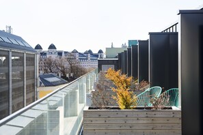 A rooftop terrace with a glass balustrade, a wooden planter with a small tree, and a row of green chairs. - Comfort Hotel Xpress Central Station (Oslo)