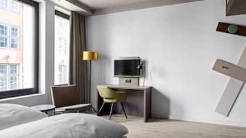 A modern hotel room with a bed, a desk, a chair, a TV, and a window with curtains.