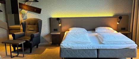 Un dormitorio moderno con una cama grande, una silla, una mesa y un televisor montado en la pared.