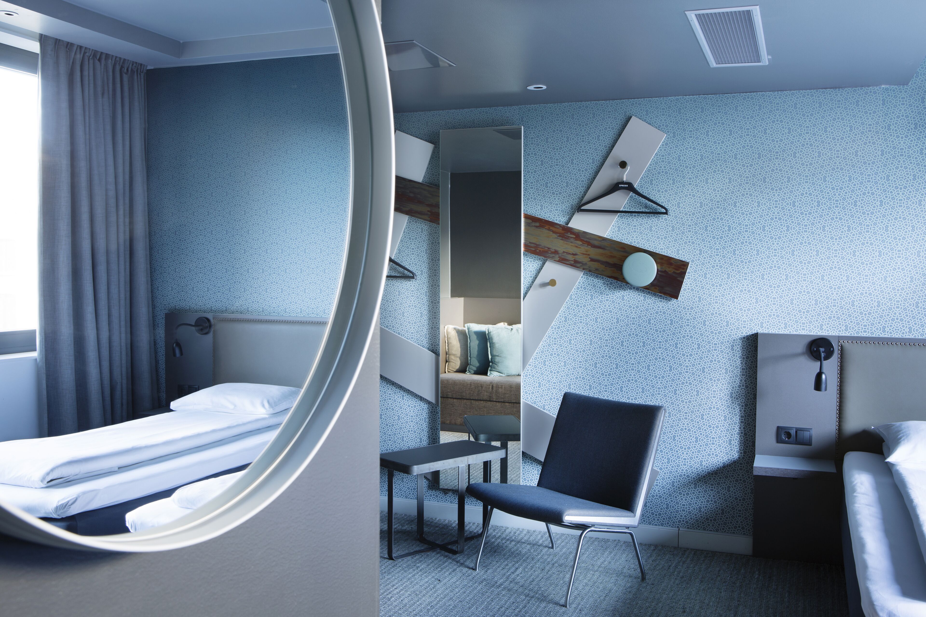 Une chambre d’hôtel moderne équipée d’un lit, d’un bureau, d’une chaise et d’un grand miroir.