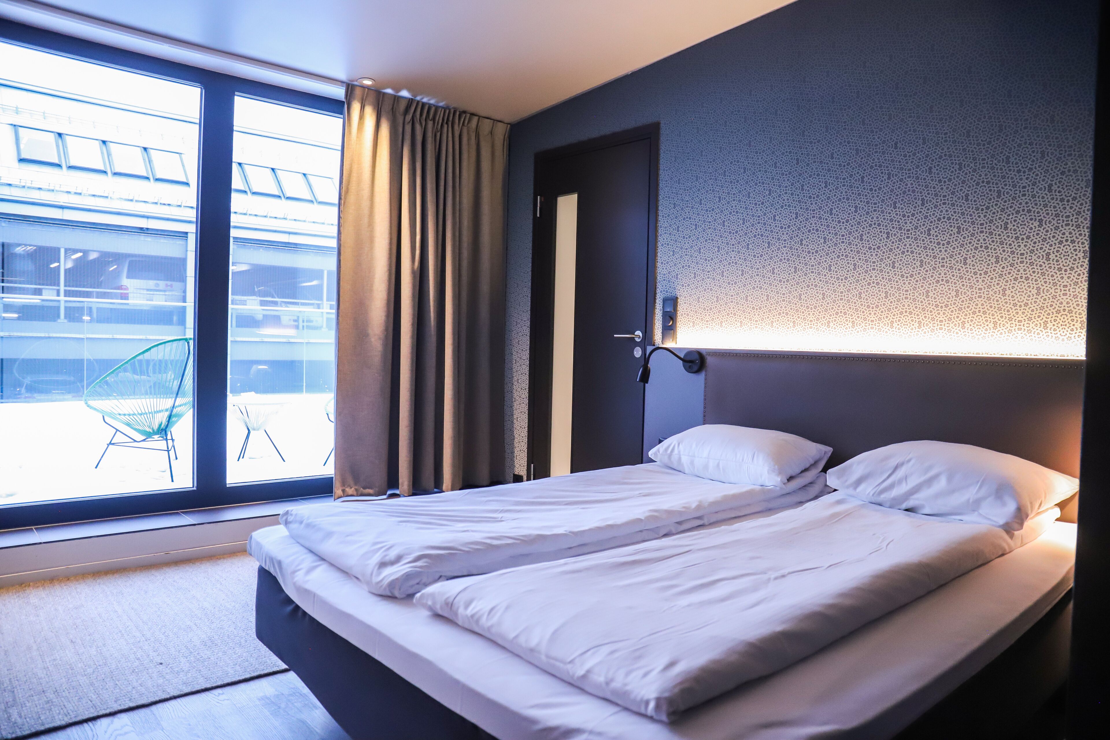 A modern hotel room with a large bed, a door, and a view of the outside.