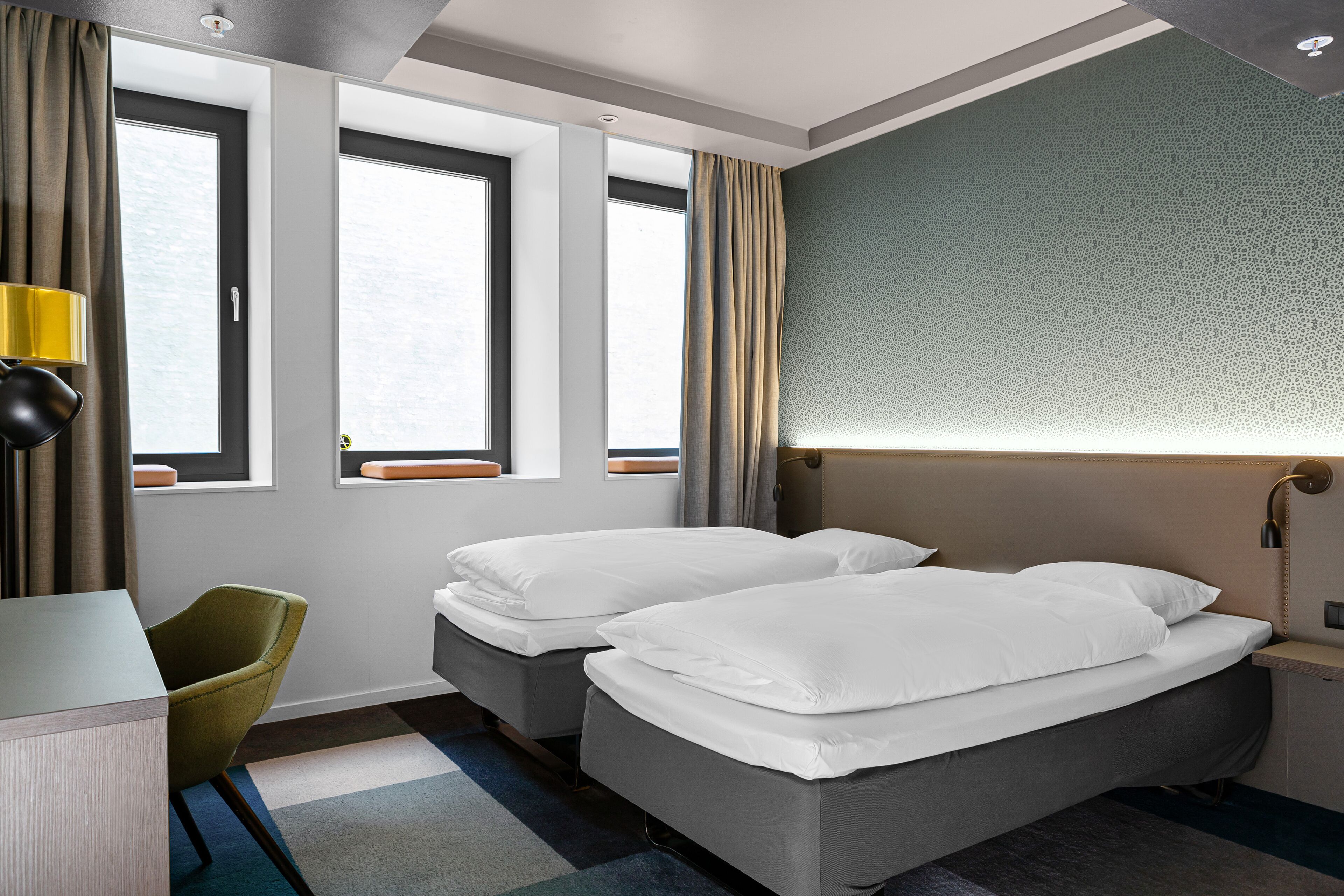 Ein Hotelzimmer mit zwei Betten, einem Schreibtisch, einem Stuhl und großen Fenstern.