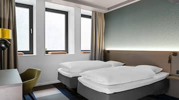 Ein Hotelzimmer mit zwei Betten, einem Schreibtisch, einem Stuhl und großen Fenstern.