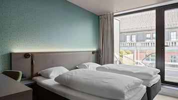 Habitación de hotel con una cama grande, un escritorio y vistas a la ciudad a través de un ventanal corredero.