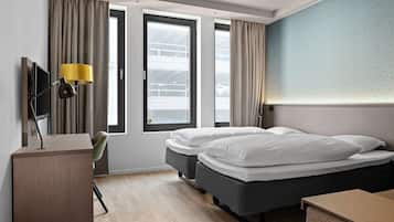 Une chambre d’hôtel avec un lit, un bureau, une chaise, une télévision et de grandes fenêtres avec des rideaux.