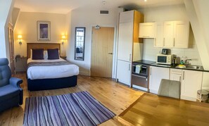 A bedroom with a bed, bedside lamps, a desk, and a chair. Adjacent is a kitchenette with a microwave, toaster, and sink. - Royal Athenaeum Suites (Aberdeen)