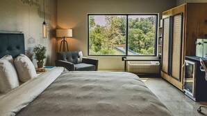 A bedroom with a large bed, a chair, a desk, a lamp, and a window with a view of trees. - Royal Athenaeum Suites (Aberdeen)