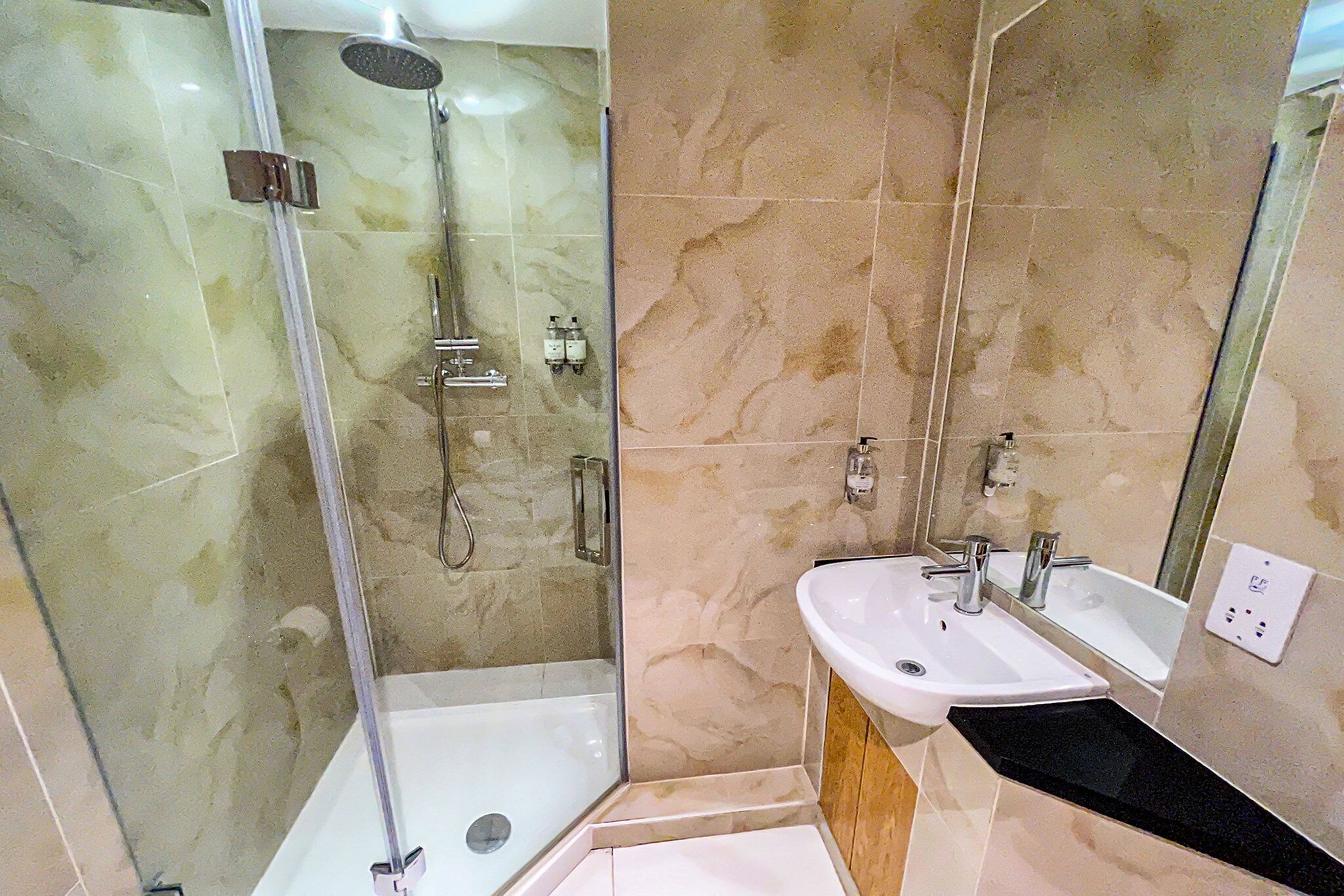 Un baño moderno con ducha envuelta en vidrio, lavamanos blanco y espejo.