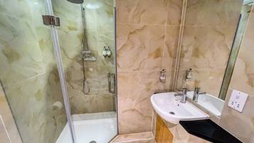 Un baño moderno con ducha envuelta en vidrio, lavamanos blanco y espejo.