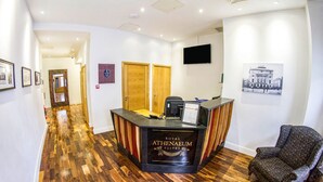 A reception desk labeled "Royal Athenaeum Suites" with a wooden floor, a mounted television, and framed pictures on the walls. - Royal Athenaeum Suites (Aberdeen)