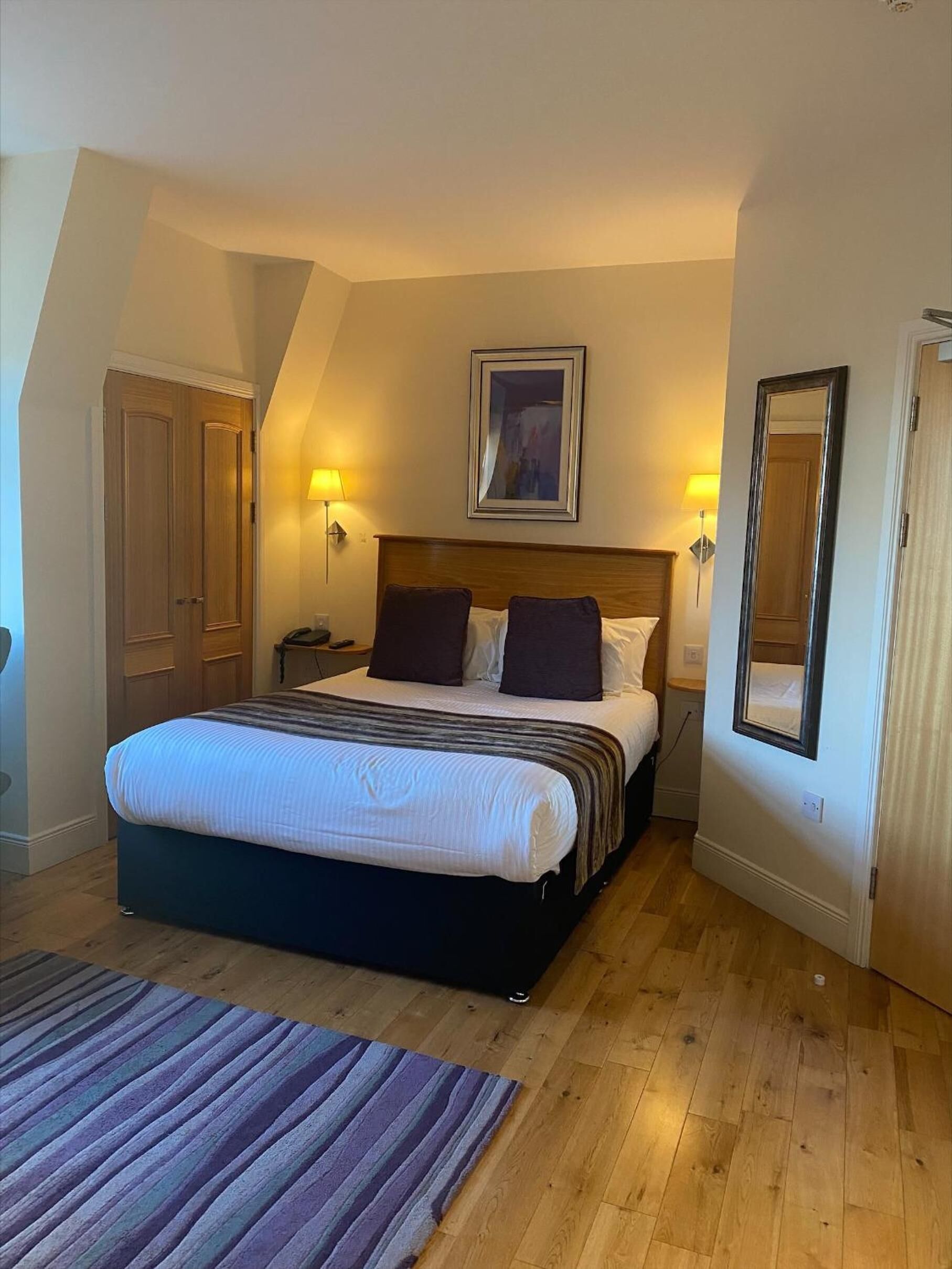 A bedroom with a large bed, two bedside lamps, a framed picture above the bed, and a mirror on the wall.