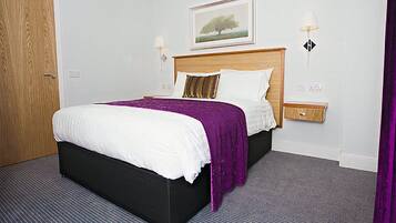 A hotel room with a large bed, a wooden headboard, a nightstand, and a framed picture on the wall.