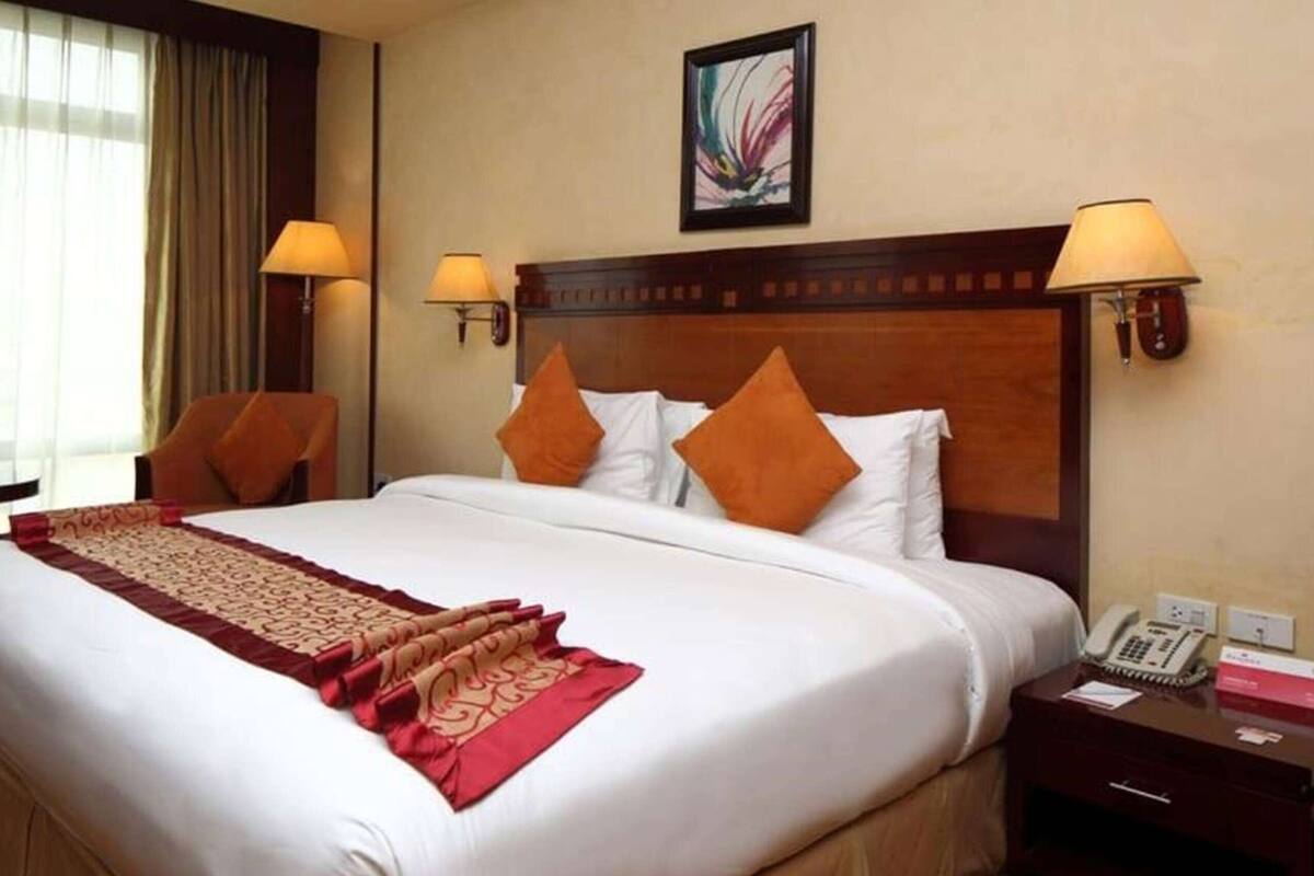 Habitación de hotel con una cama grande, dos almohadas, una mesita de noche con lámpara y un cuadro en la pared.