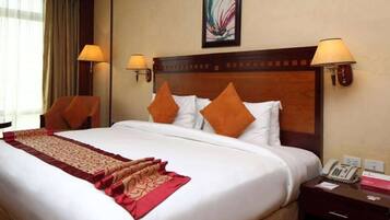 A hotel room with a large bed, two pillows, a bedside table with a lamp, and a painting on the wall.