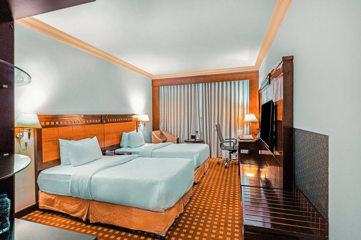 Habitación de hotel con dos camas, un escritorio, una silla, un televisor y una ventana con cortinas.