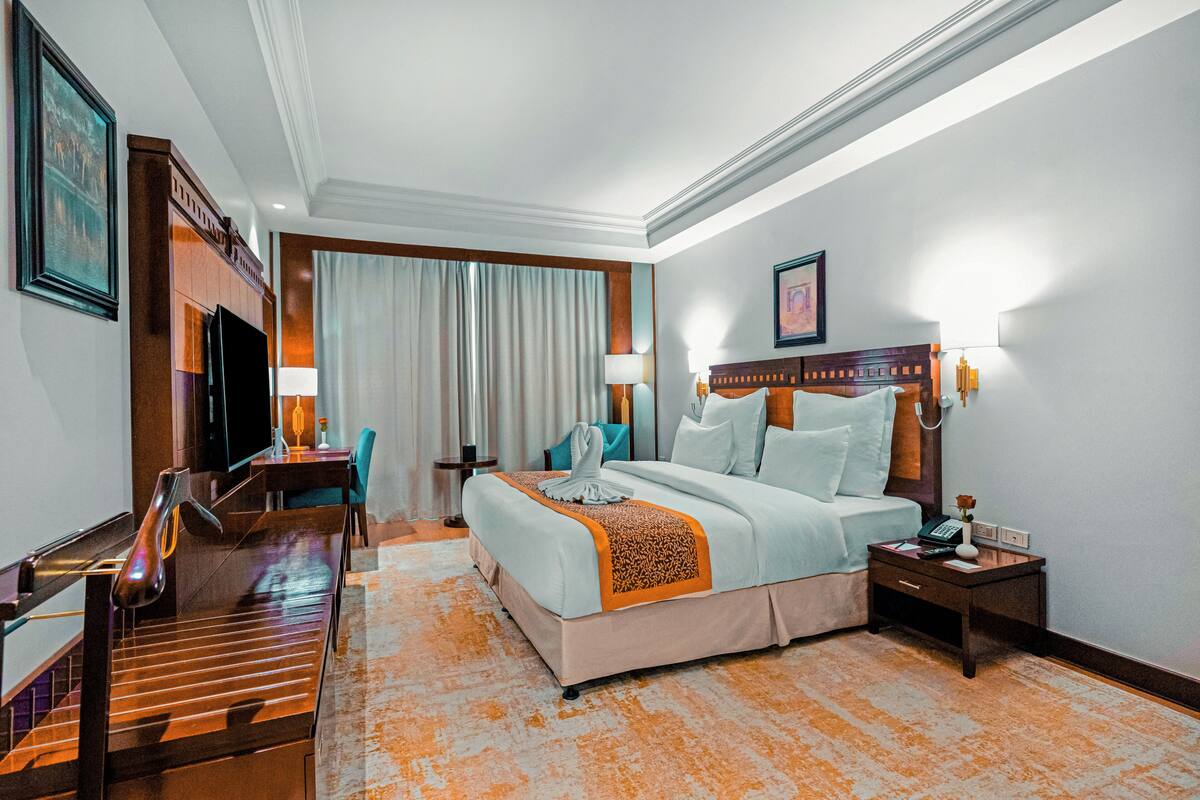 Habitación de hotel con cama, escritorio, silla, televisor y lámpara.