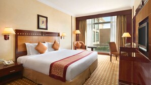 A hotel room with a large bed, two bedside lamps, a desk with a telephone, a TV, and a view of the outdoors through a large window. - Ramada by Wyndham Riyadh (Riyadh)