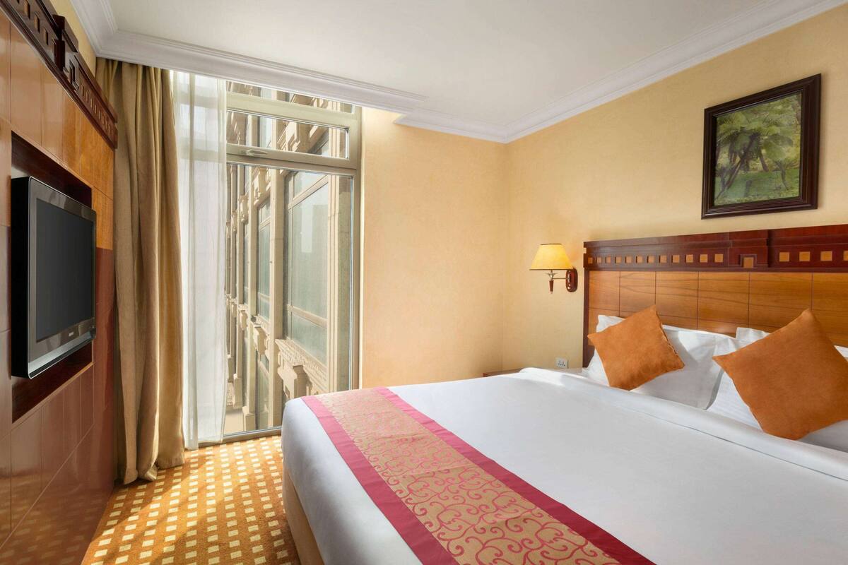 Habitación de hotel con una cama grande, televisión, ventana con cortinas y un cuadro en la pared.