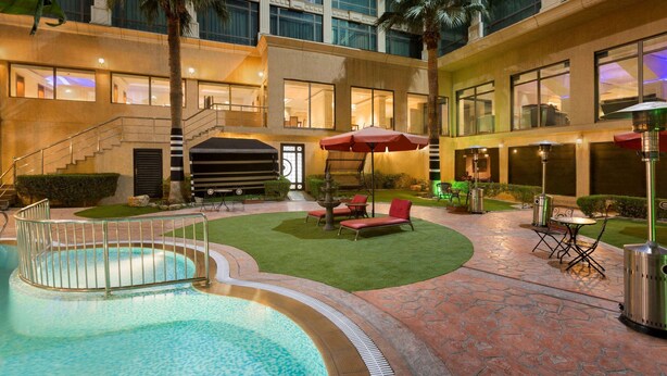 A hotel courtyard with a swimming pool, outdoor seating, and a staircase leading to an upper level. - Ramada by Wyndham Riyadh (Riyadh)