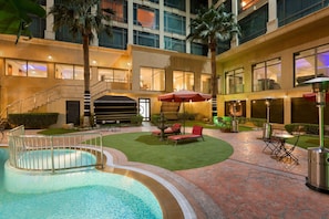 A hotel courtyard with a swimming pool, outdoor seating, and a staircase leading to an upper level.