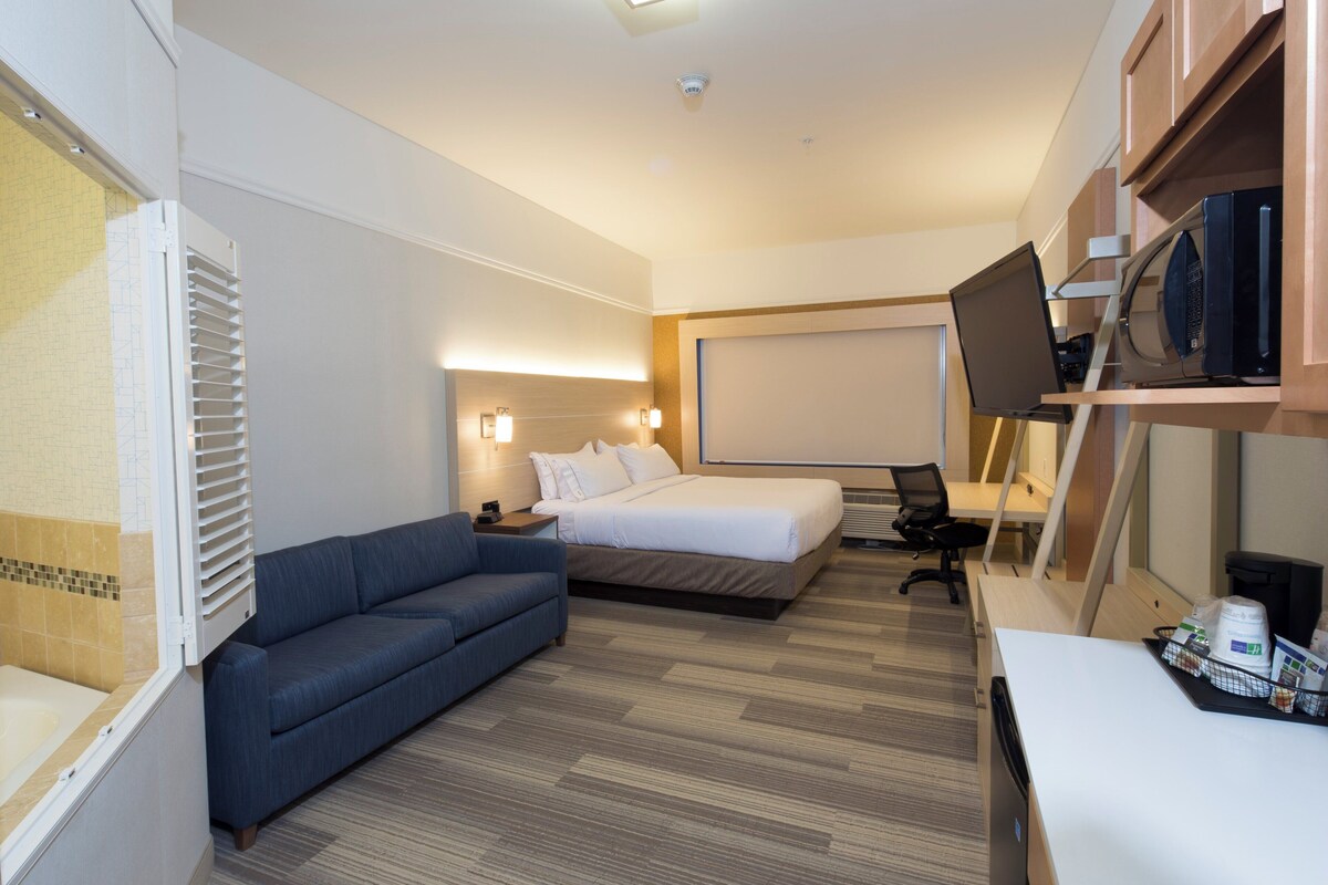 A hotel room with a bed, a sofa, a desk with a computer, a TV, and a microwave.