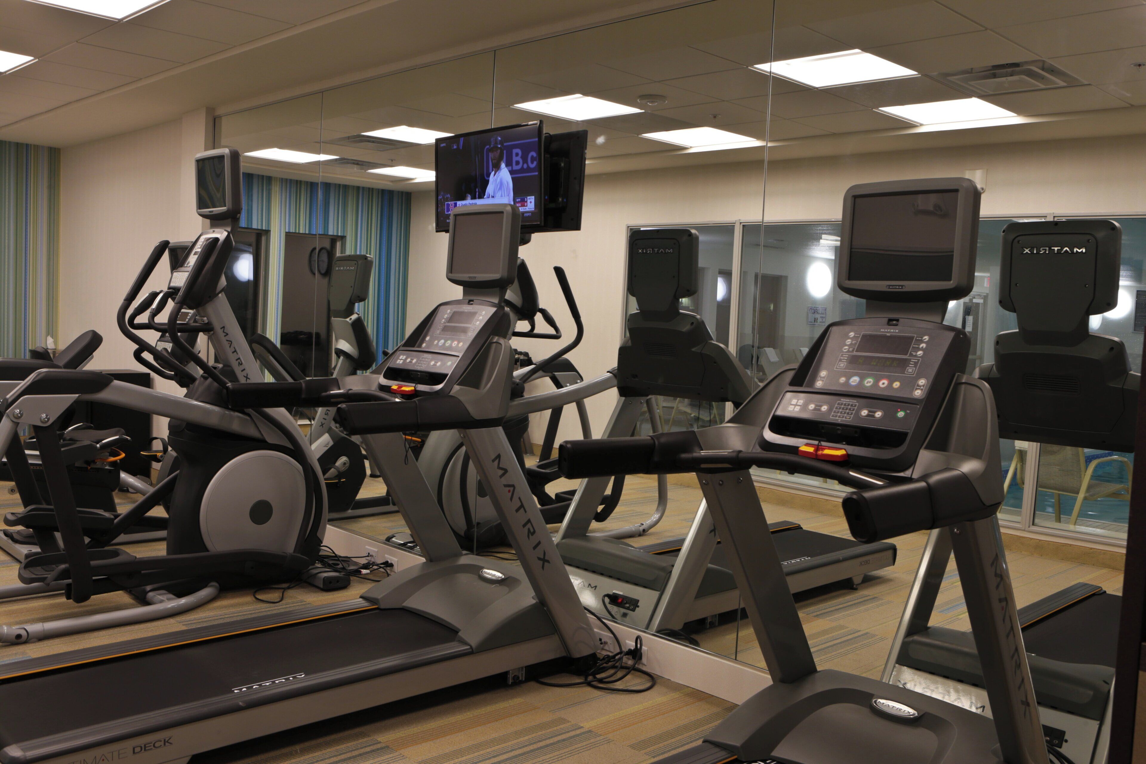 A gym with treadmills, stationary bikes, and a television mounted on the wall.