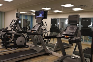 Un gimnasio con cintas de correr, bicicletas estáticas y un televisor en la pared.