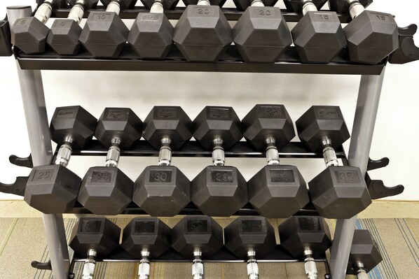 A rack of hexagonal dumbbells with weight markings, arranged in rows on a metal stand.