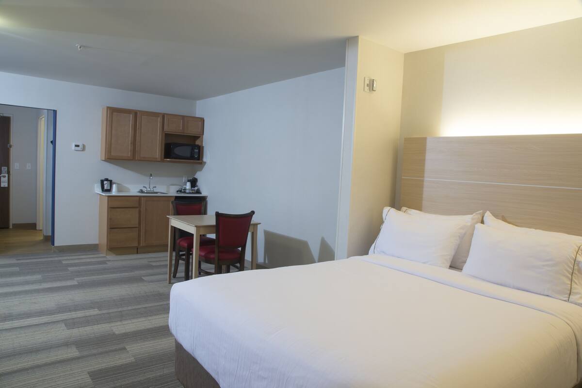 Habitación de hotel con cama, escritorio, silla y kitchenette.