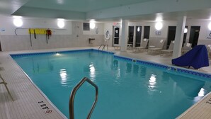 Una piscina interior con agua cristalina, un trampolín y sillas de descanso alrededor del borde.