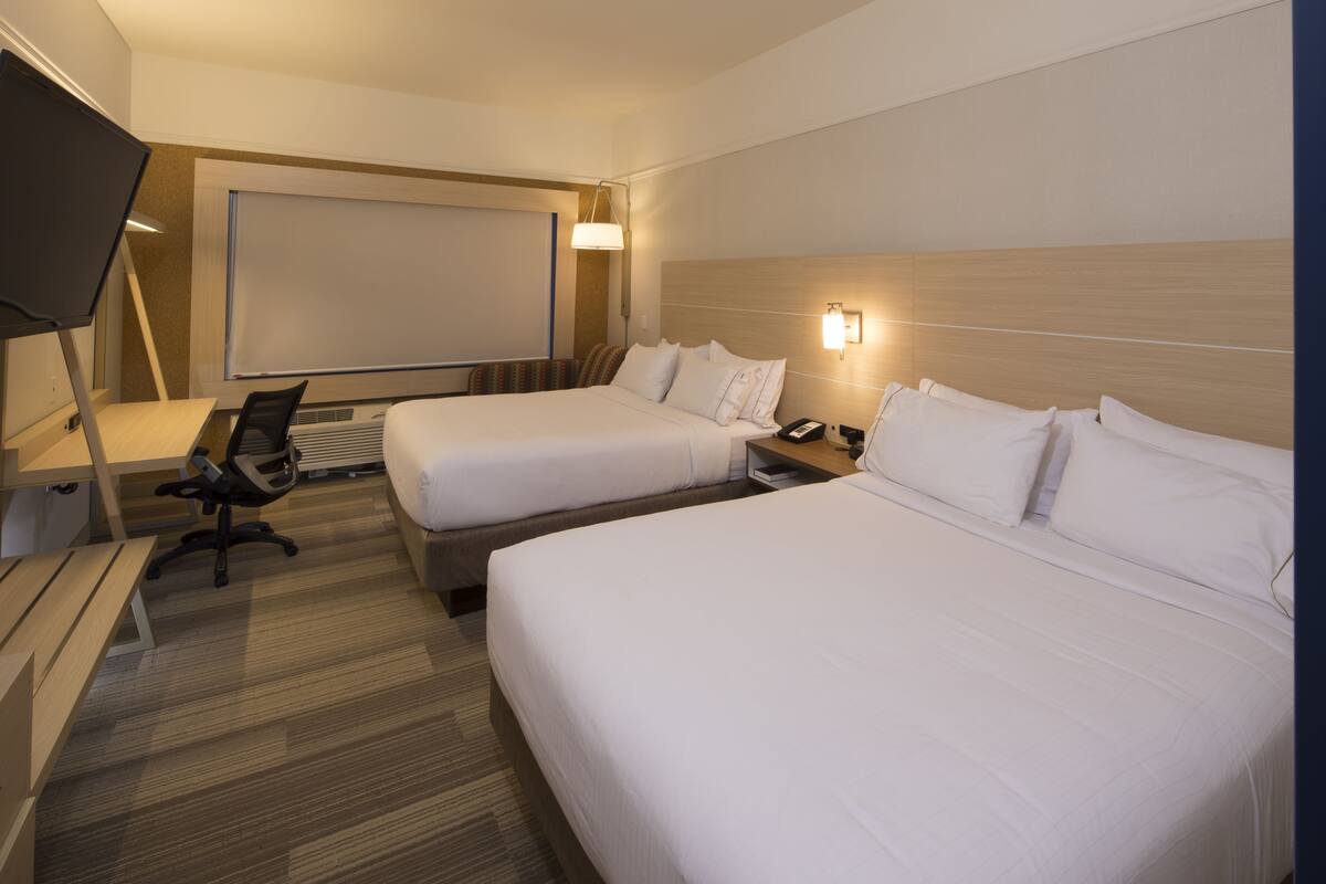 Habitación de hotel con dos camas, un escritorio, una silla, un televisor y una lámpara fijada a la pared.