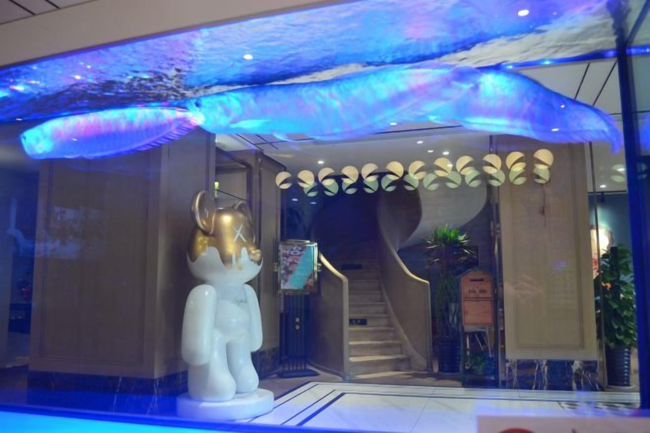 A hotel lobby with a large white statue, a staircase, and a ceiling with a wave-like design.