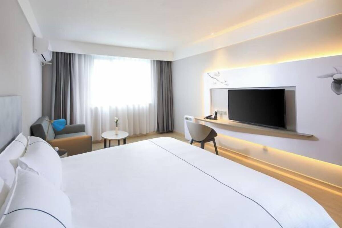 A hotel room with a large bed, a TV mounted on the wall, a small table, and a chair.