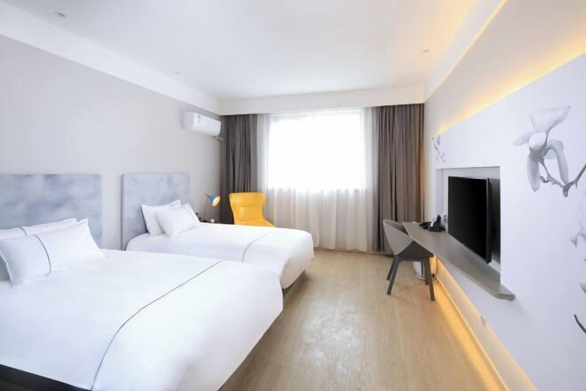 A hotel room with two beds, a flat-screen TV, a chair, and a large window with curtains.