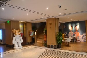 Un hall d’hôtel avec une grande statue d’ours, un escalier et un espace repas comprenant des chaises et des tables.