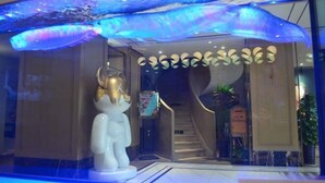 Un hall d’hôtel avec une grande statue blanche, un escalier et un plafond orné de motifs ondulés.