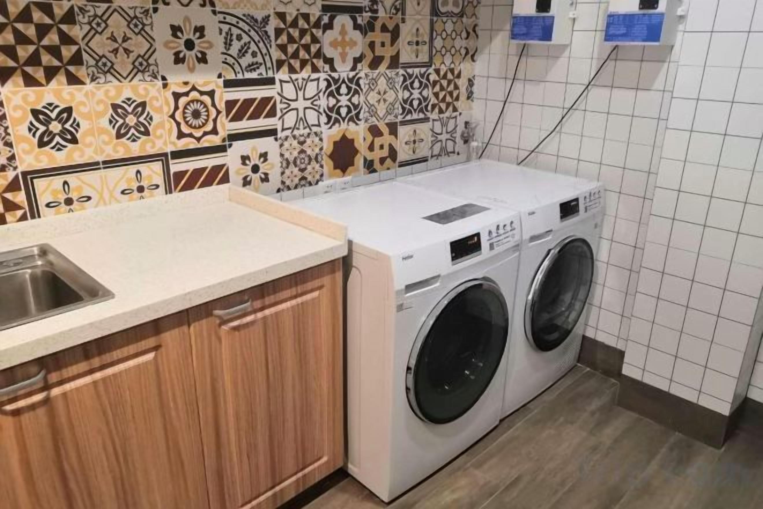 A laundry area with a washing machine, a sink, and patterned tiles on the wall.