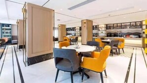 Un espace repas moderne avec des tables et des chaises rondes, une cuisine en arrière-plan et un sol à motifs.
