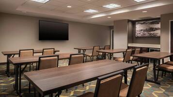 A conference room with multiple tables and chairs, a flat-screen TV mounted on the wall, and a patterned carpet.