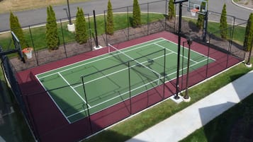 An outdoor tennis court with a red surface, surrounded by a black fence, and equipped with multiple light poles.