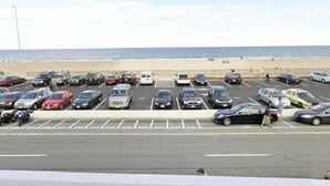 A parking lot with cars and a beach in the background. - Atlantic Sands (Hampton)