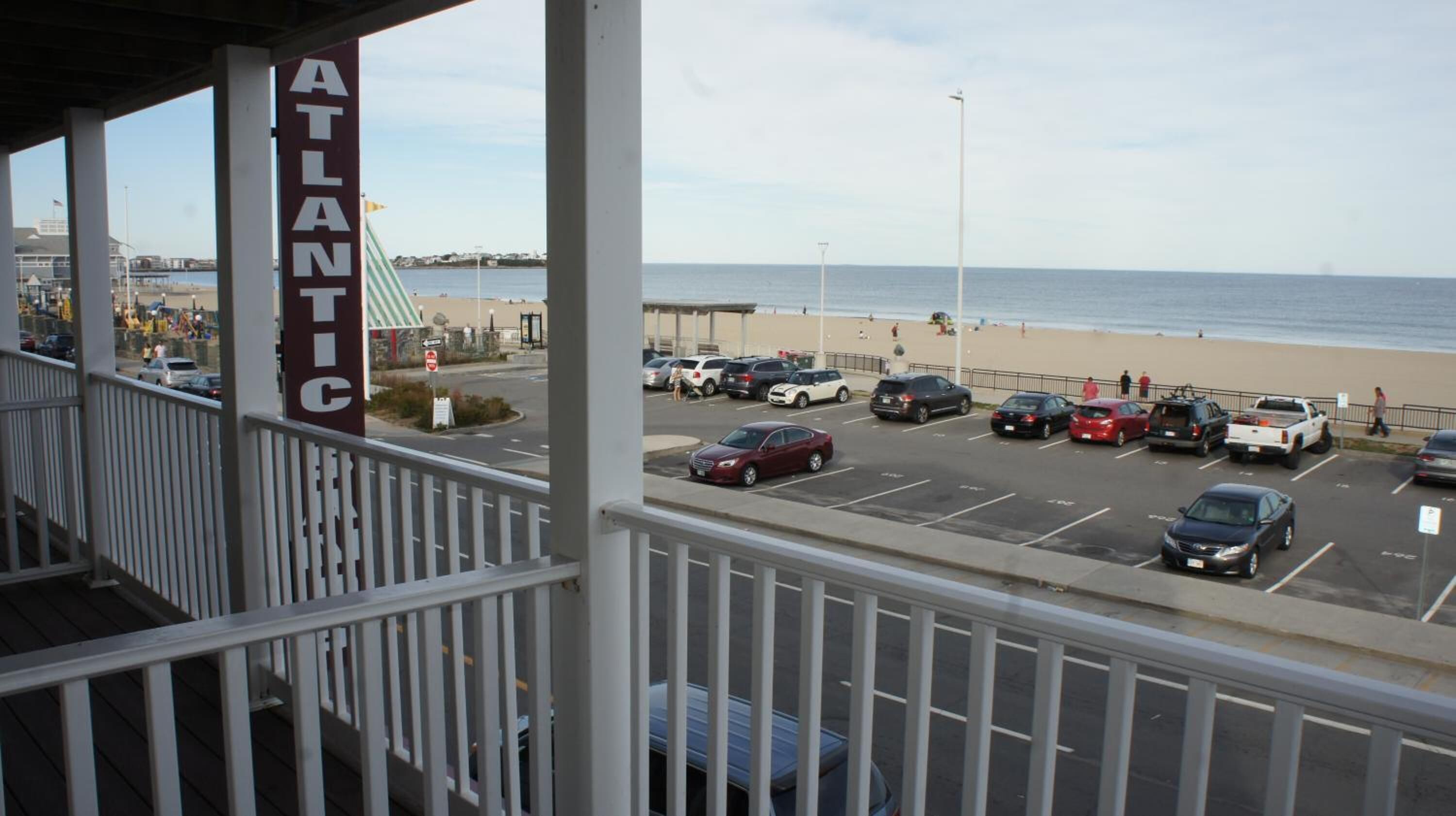 A view from a balcony overlooking a parking lot with a beach and ocean in the background.