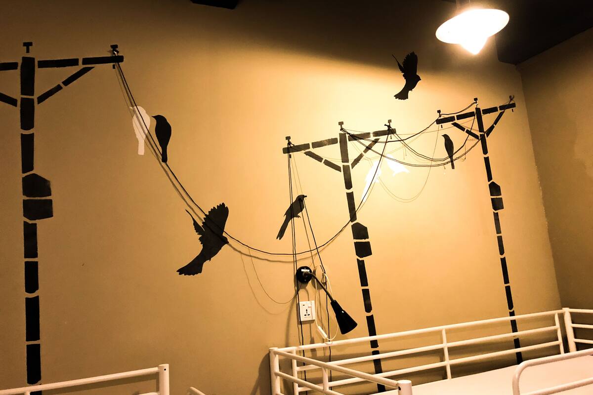 A room with a bed, a white railing, and a wall with a power outlet and a lamp.