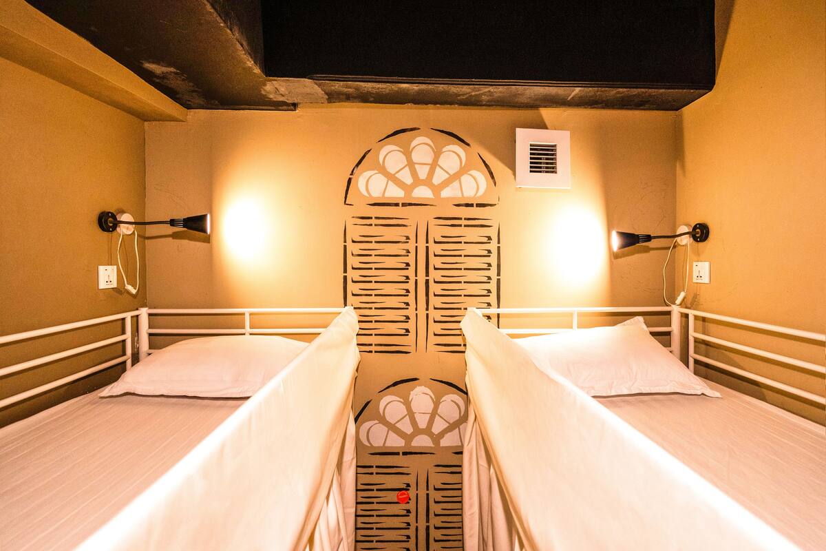A room with two single beds, a decorative wall panel, and a wall-mounted air conditioning unit.
