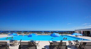 A swimming pool with blue umbrellas, lounge chairs, and a view of the ocean.