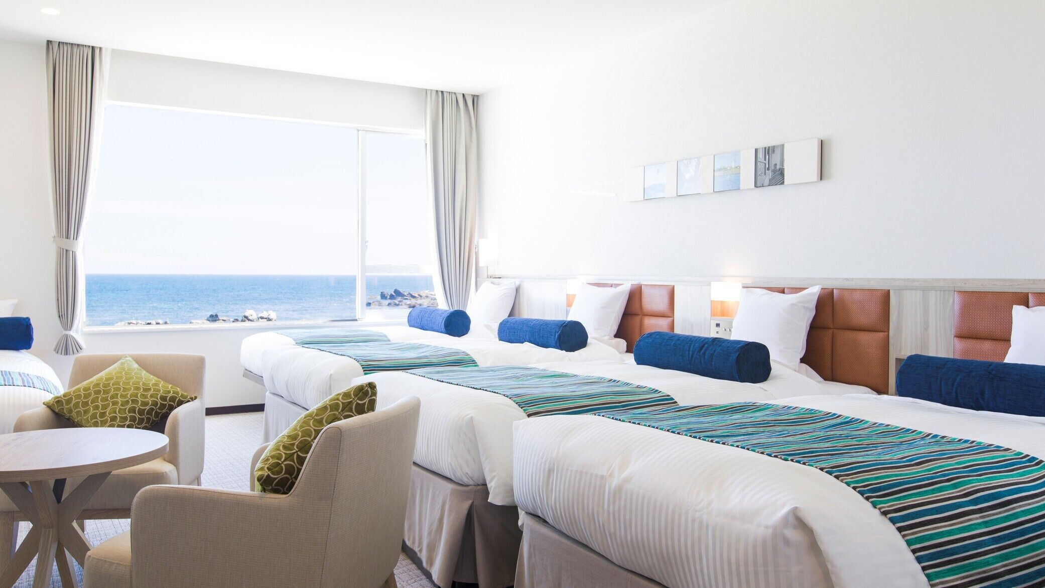 Ein Hotelzimmer mit zwei Betten, einem kleinen Tisch und Meerblick.