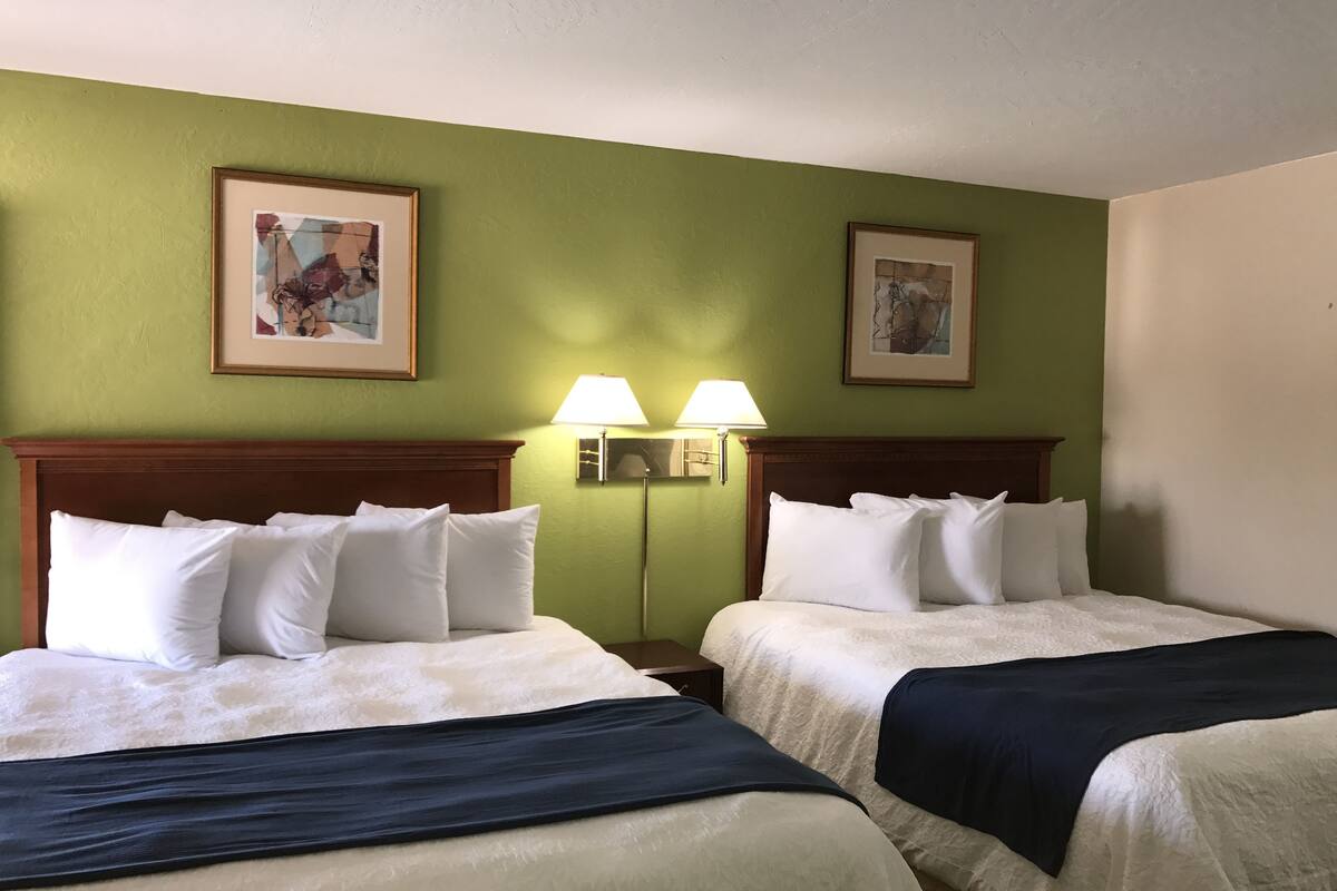 A hotel room with two beds, green walls, and framed artwork.